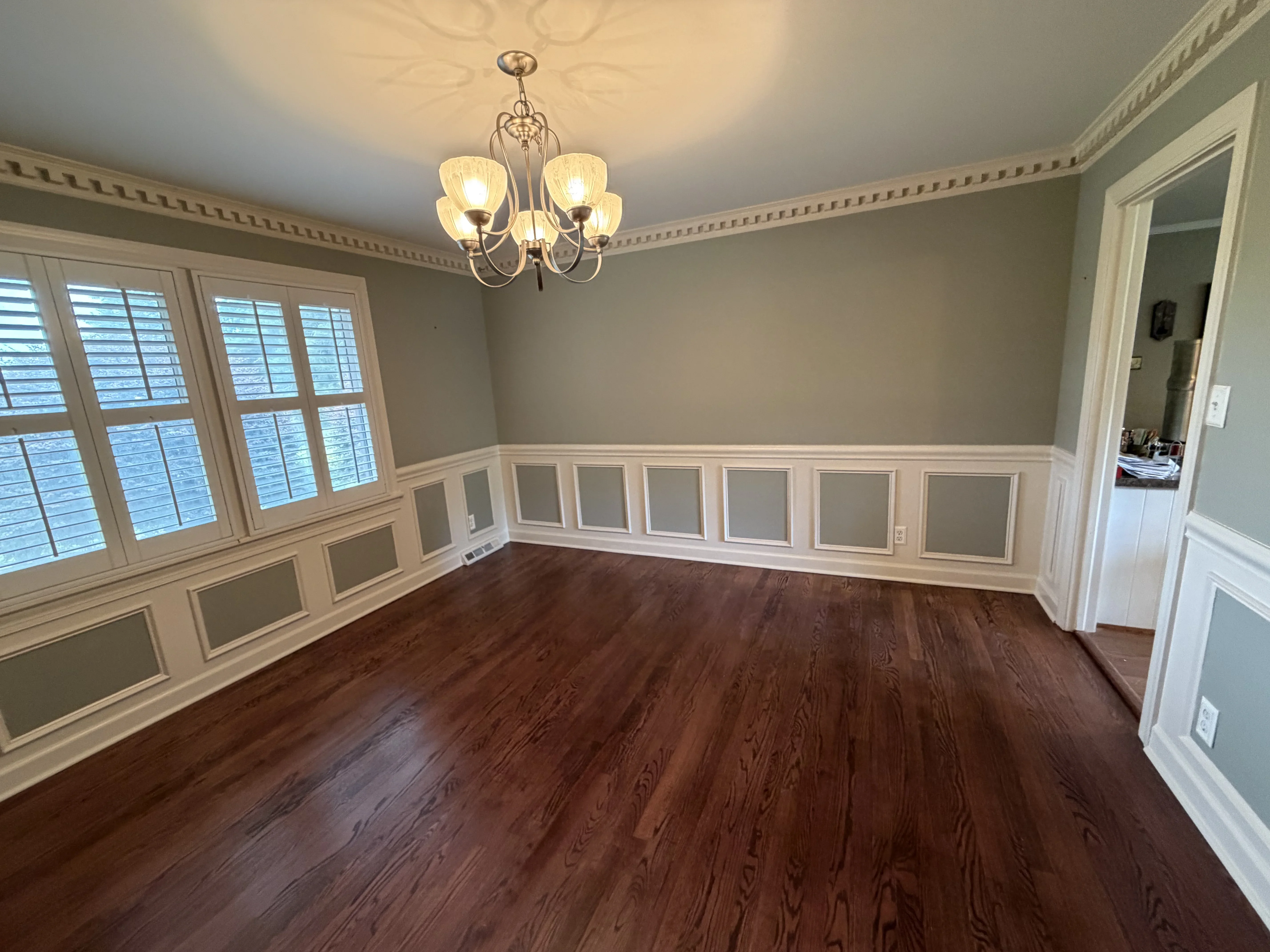 Formal dining room with white wainscoting, sage green walls, crown molding, and hardwood floors