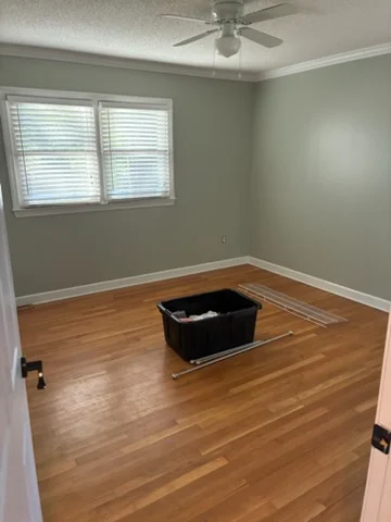 Empty bedroom with sage green painted walls, white crown molding and baseboards, and warm hardwood floors