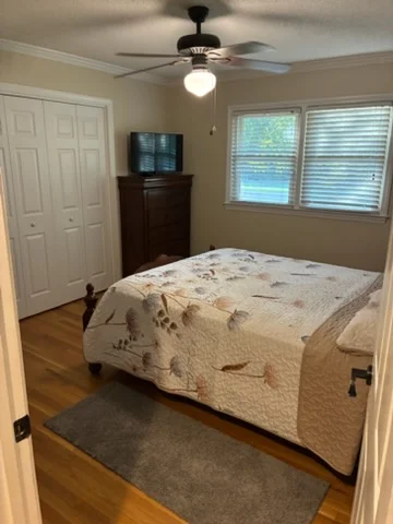 Bedroom with neutral painted walls, white trim and closet doors, crown molding, and hardwood floors