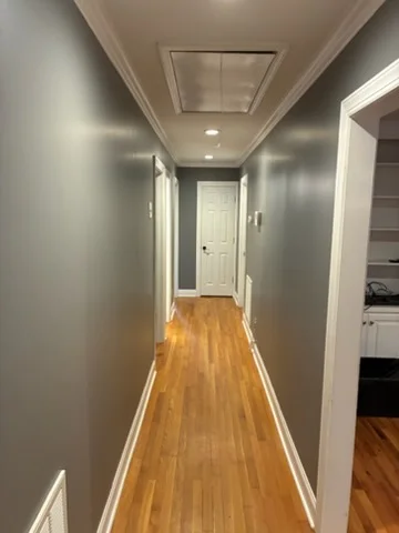 Long hallway with gray painted walls, white crown molding and baseboards, and refinished honey-toned hardwood floors