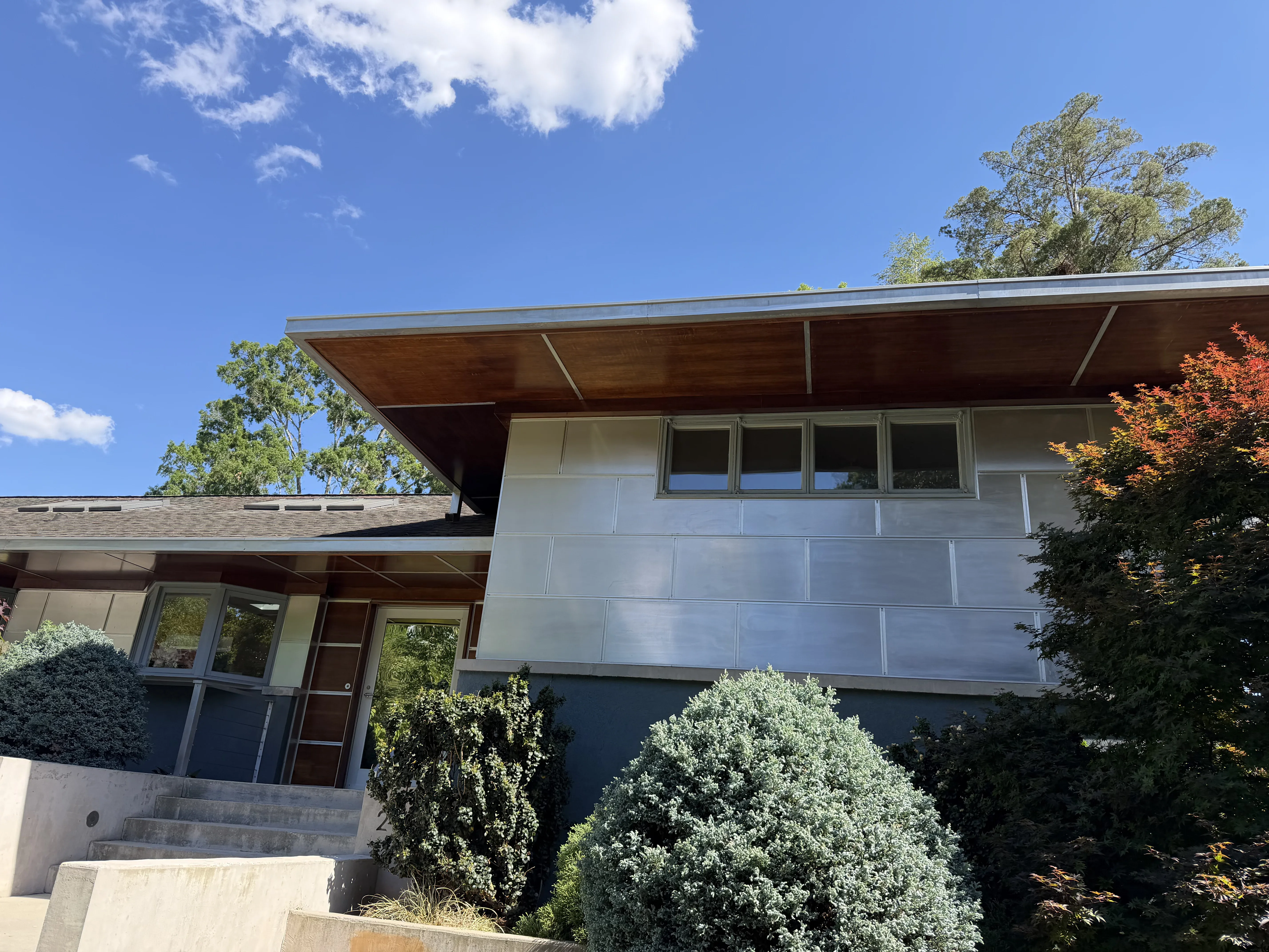 Mid-century modern home with light gray upper facade, dark charcoal lower wall, and wood soffit overhang