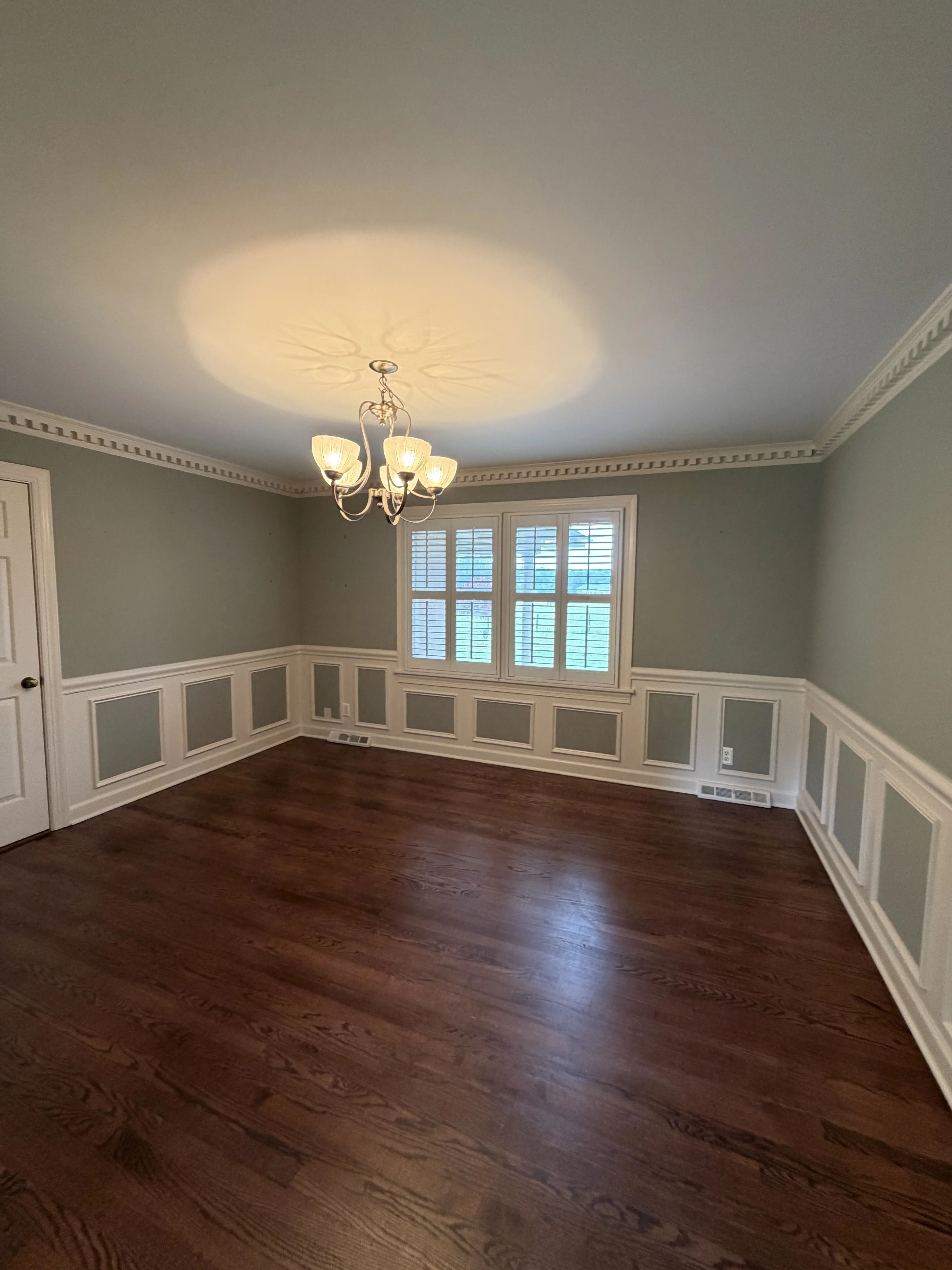 Sage green walls with white wainscoting, painted ceiling, hardwood floor, and shuttered windows