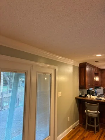 Sage green painted kitchen walls with white crown molding, glass French doors, and wood floor near stained cabinetry
