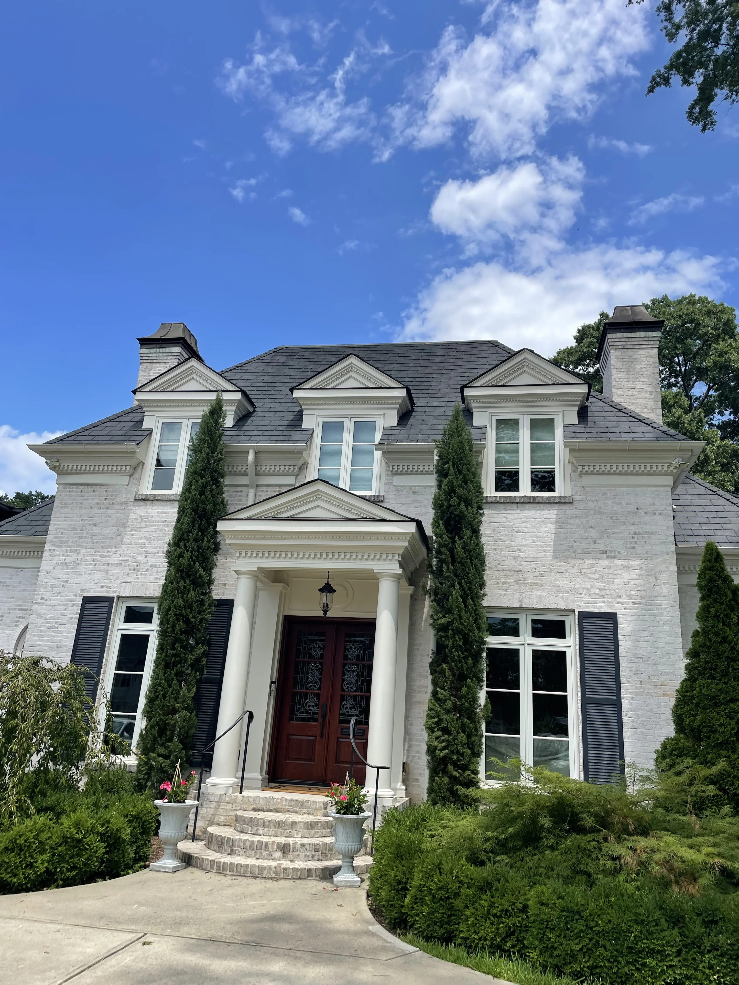 White brick home with painted trim, shutters, and classical entry portico featuring dark red double doors