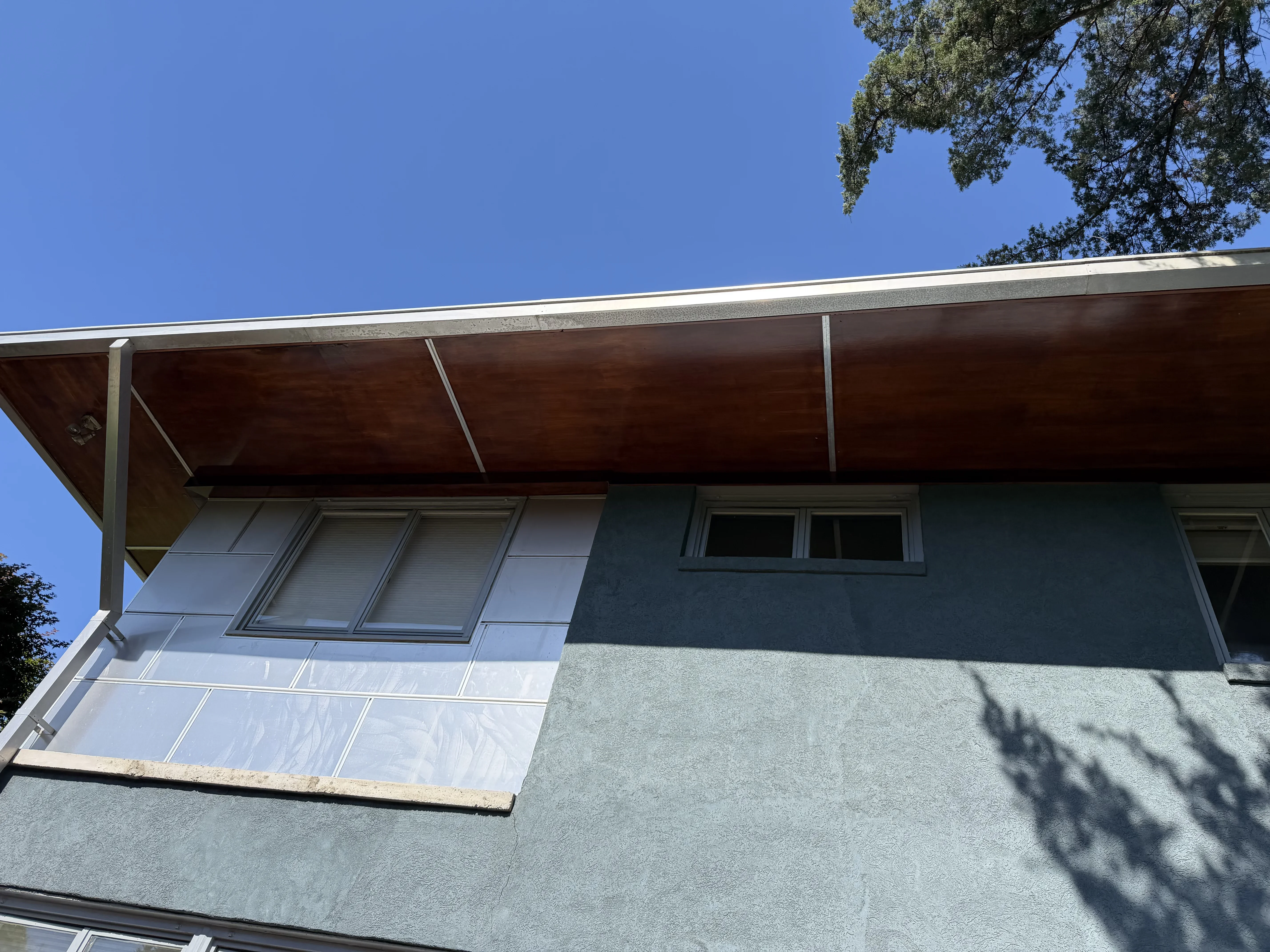 Exterior home with gray stucco walls, white trim, and dark metal overhang structure