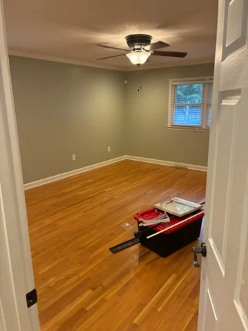 Sage green Charlotte room with white window trim, baseboards, and a ceiling fan after painting